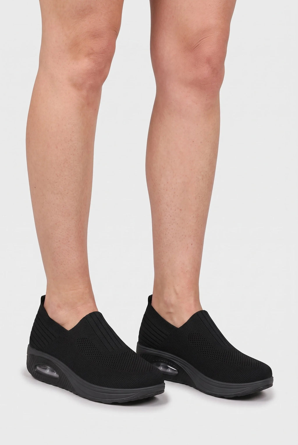 Front view of model's lower legs wearing black knit slip-on trainers with wedge platform soles