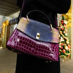 Woman carrying the purple and burgundy handbag on her shoulder outdoors near festive lights