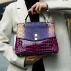 Close-up of a woman holding the purple and burgundy bag by its top handle while wearing a beige coat