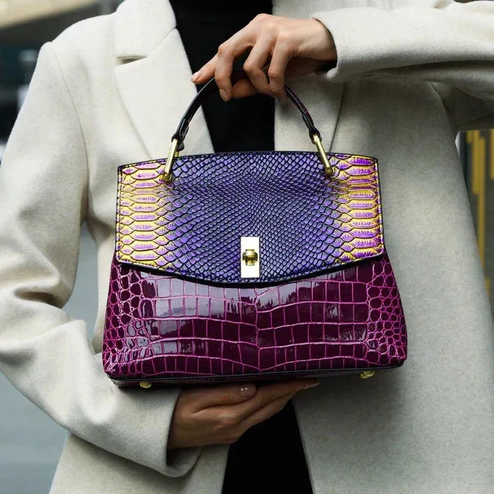 Close-up of a woman holding the purple and burgundy bag by its top handle while wearing a beige coat
