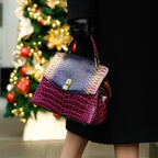 Woman holding the purple and burgundy bag by its top handle against a black outfit outdoors