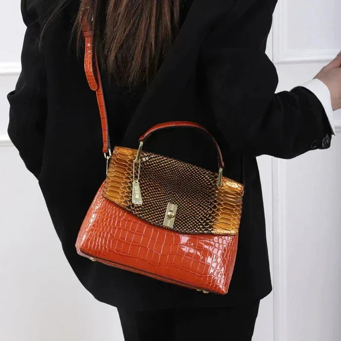 Woman wearing a black blazer carrying the orange and gold bag crossbody over one shoulder