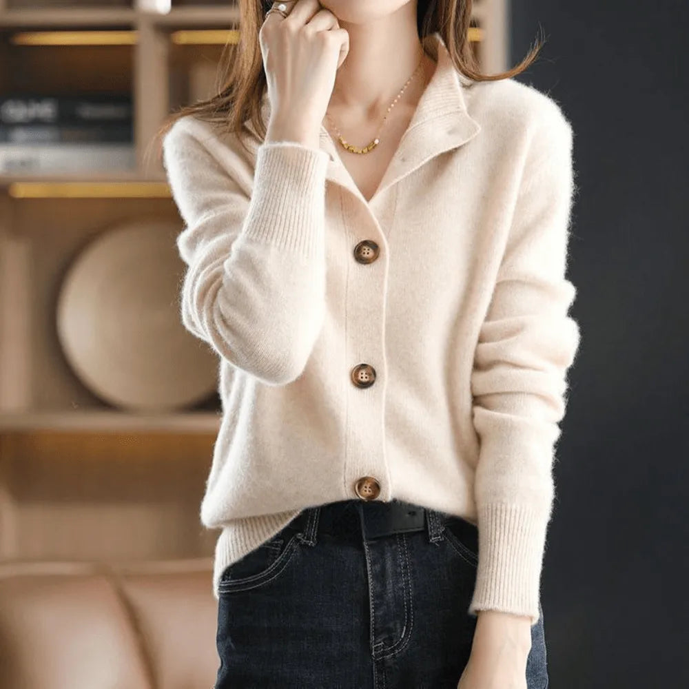 Cream cashmere cardigan showing ribbed cuffs and notched collar detail, hand raised to the chin