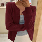 Burgundy knitted cardigan with round neckline and button front, worn open over layered tops