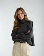 Close front view of the charcoal grey jumper with arms crossed, showing the ribbed polo neck and piped shoulder seams