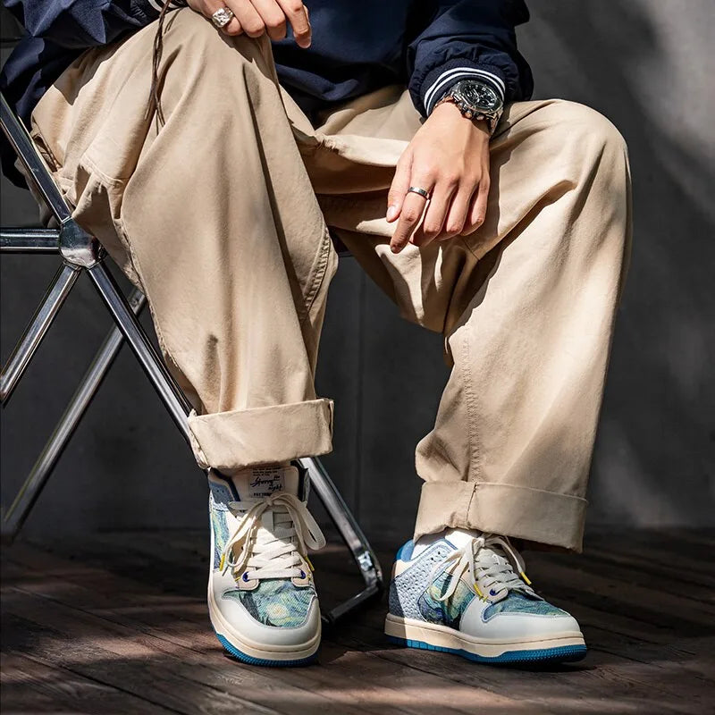 Man seated wearing hi-top style art print trainers paired with rolled beige trousers and a navy jacket