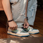 Close-up of a hand tying the cream laces of the Starry Night panel trainer against light denim