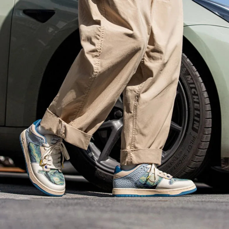 Man walking beside a car wheel wearing the cream and teal art print trainers with cuffed trousers