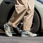 Man walking beside a car wheel wearing the cream and teal art print trainers with cuffed trousers