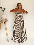 Strapless bandeau maxi dress in brown and white stripe worn against a plain wall, full length front view