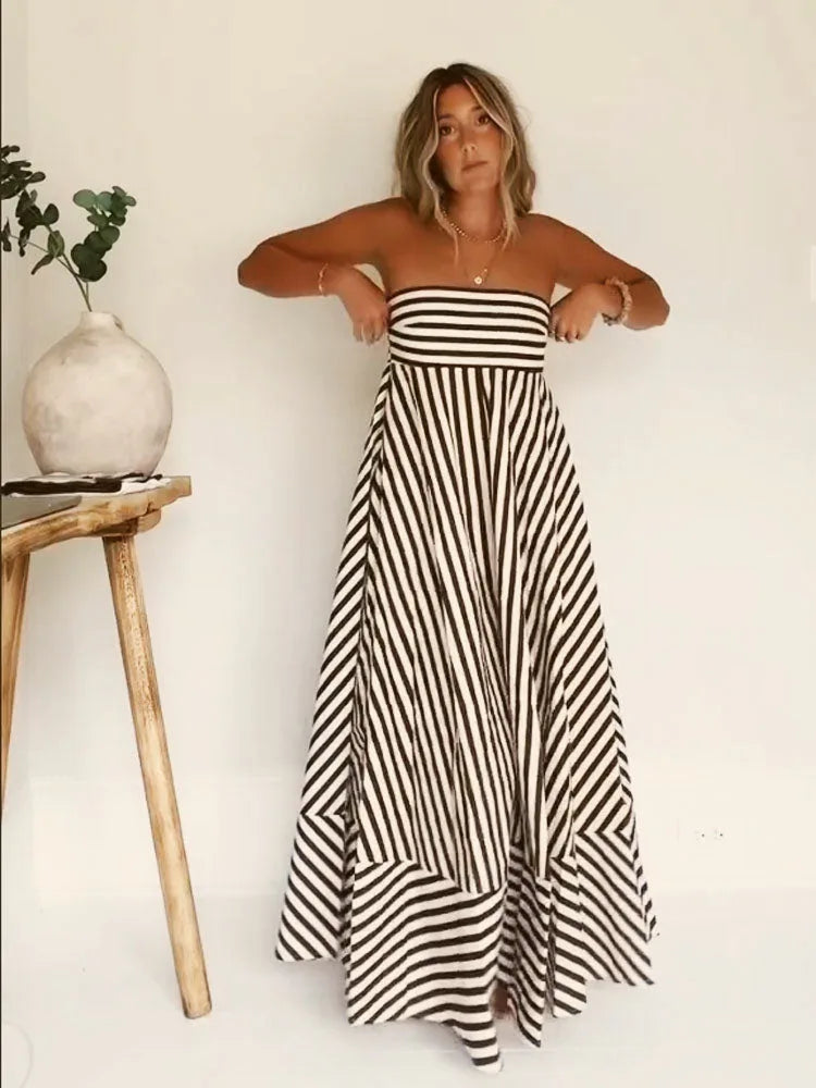 Strapless bandeau maxi dress in brown and white stripe worn against a plain wall, full length front view