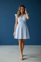 Woman wearing a blue and white striped V-neck skater dress with flutter sleeves, standing against a dark blue backdrop.