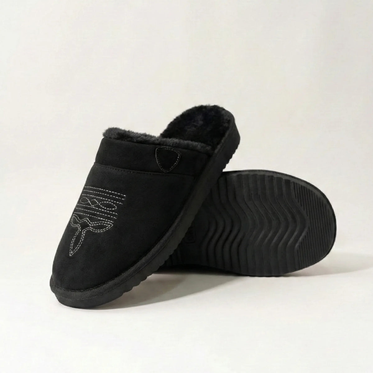 Three-quarter view of black suede slipper with tan cuff and embroidered toe stitching