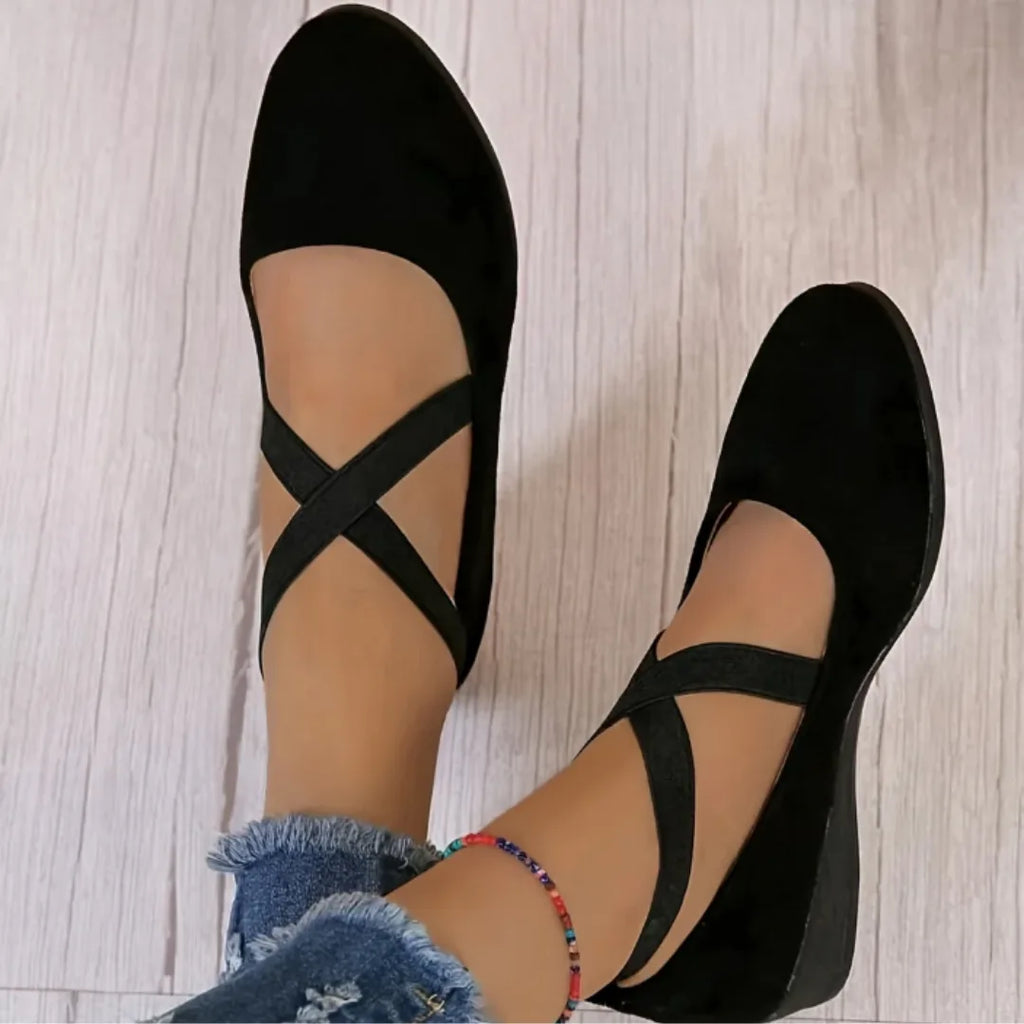 Overhead view of black suede ballet flats with crisscross elastic ankle straps worn with cropped jeans