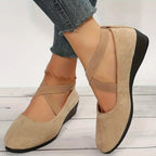 Side view of beige suede crisscross-strap ballet flats worn with cropped denim, showing low wedge sole