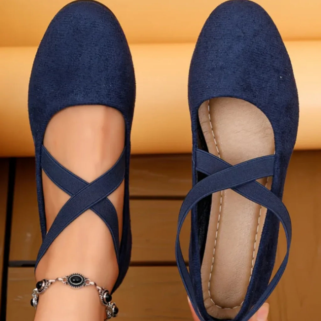 Pair of navy blue suede ballet flats shown from above and below, with crisscross straps and stitched insole