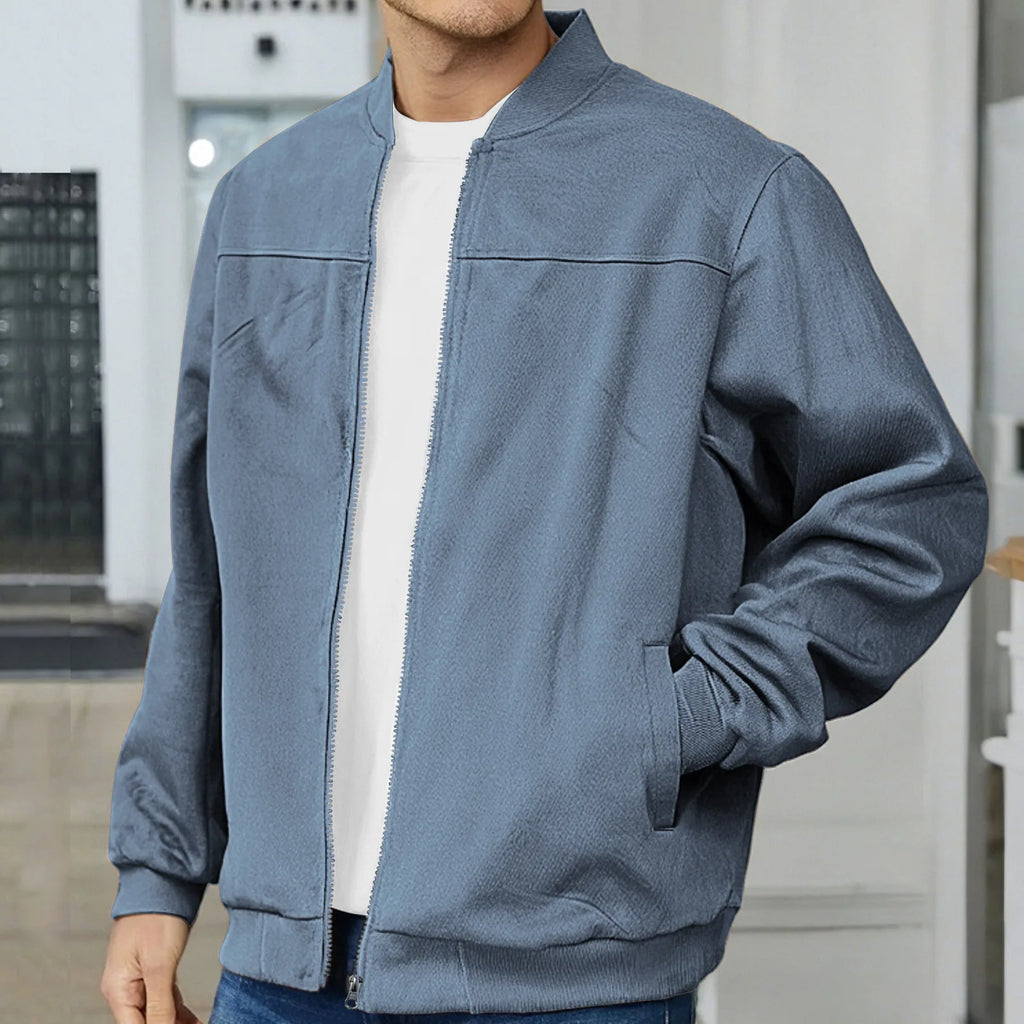 Close-up of a slate blue bomber jacket worn open over a white t-shirt, showing the ribbed collar and hand pocket