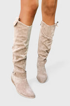 Front view of taupe suede knee-high boots with bow trim and buckle strap at the ankle