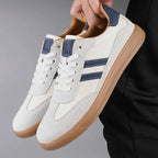 Off-white suede trainer with navy stripes held in hand, showing tan heel tab and lining