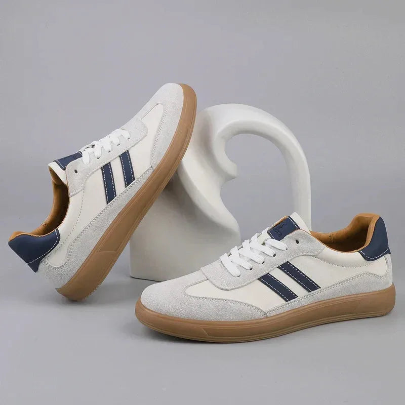 Pair of off-white suede trainers with navy stripes and gum soles resting against a curved white stand