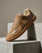Side view of brown suede and leather trainer with gum sole and tonal laces on concrete block