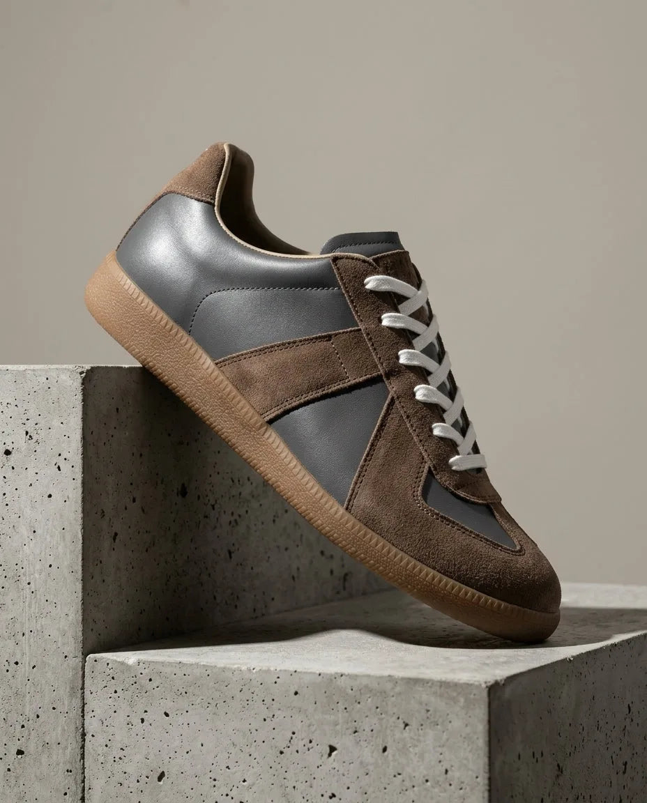 Grey leather trainer with brown suede panels and white laces, gum sole, angled side profile on stone