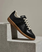 Black leather and suede trainer with cream laces and gum sole, side view on a concrete step