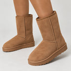 Close-up of legs wearing tan suede boots, showing the shearling-style lining at the top edge