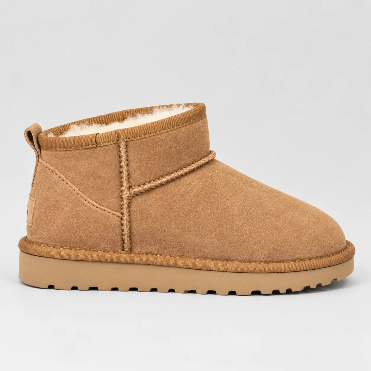 Side view of a tan suede mini ankle boot with plush cream faux-fur lining and ribbed grip sole