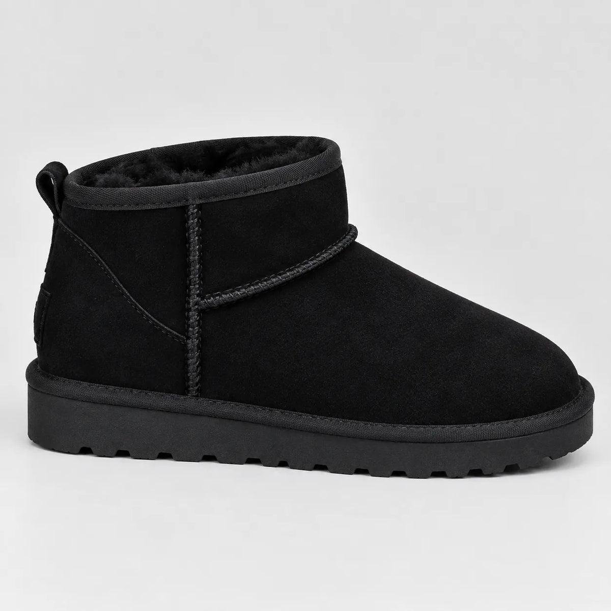 Side profile of a black suede mini ankle boot with matching stitched pull tab and chunky tread sole