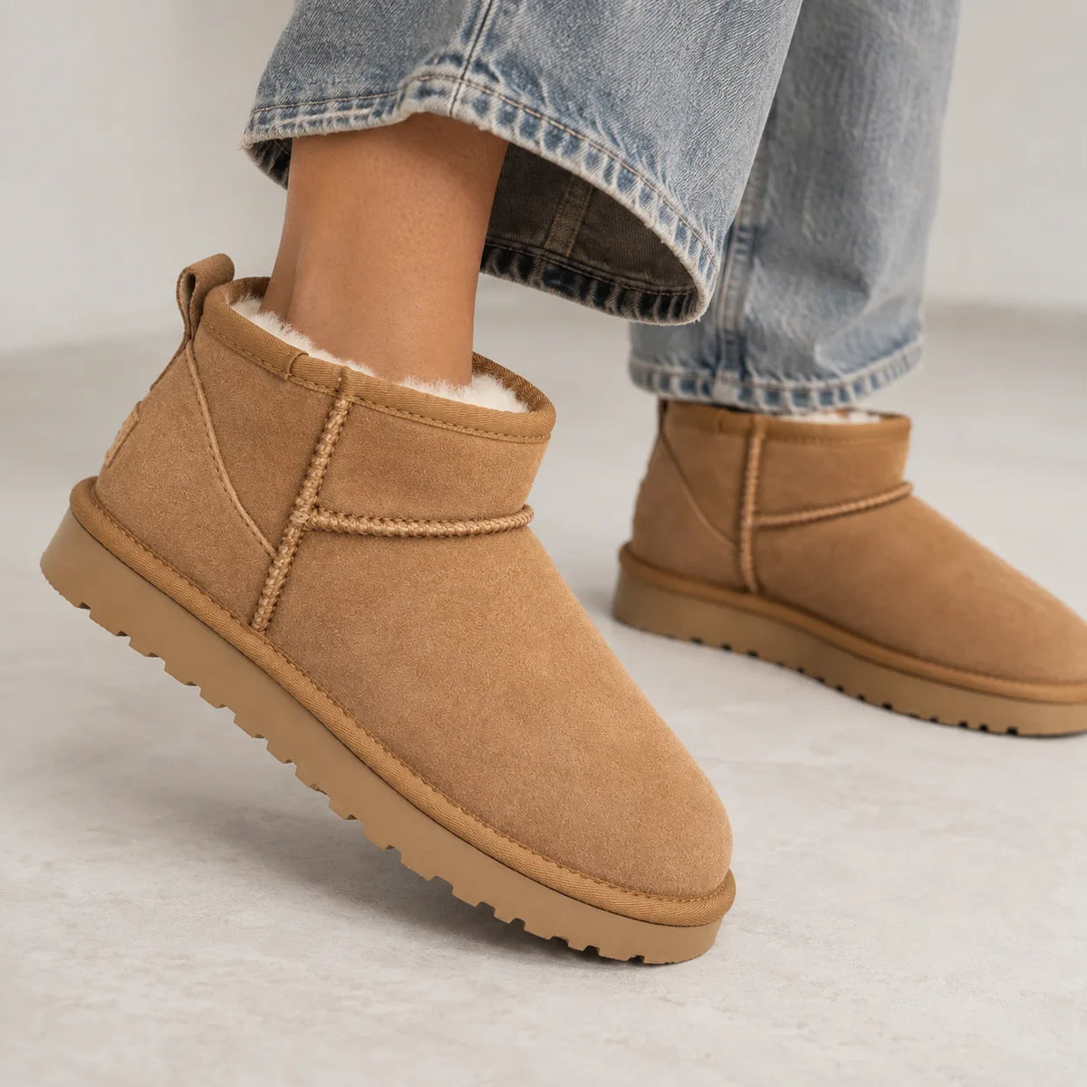 Close-up of a model wearing tan suede mini boots with wide-leg jeans, showing the fit around the ankle