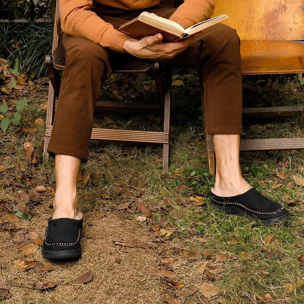 Man wearing black suede slippers outdoors while sitting and reading a book