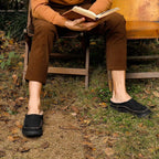 Man wearing black suede slippers outdoors while sitting and reading a book
