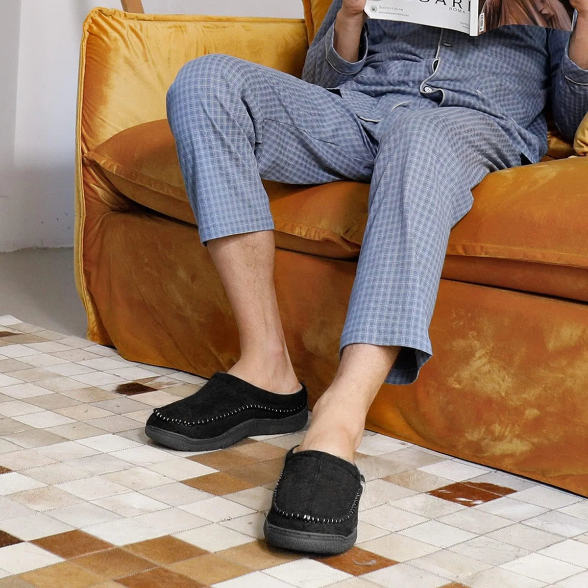 Man in pyjamas relaxing on a sofa wearing black moccasin slippers with stitched detailing