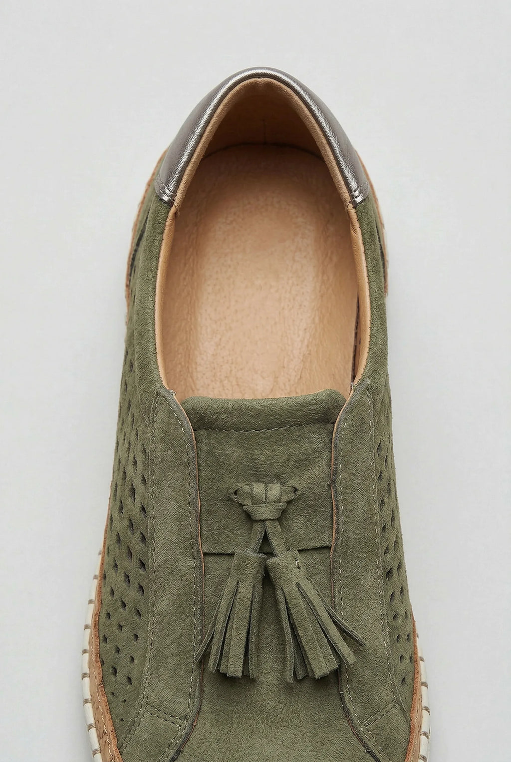 Close-up of the suede tassel trim and metallic heel tab on a green slip-on trainer, showing the tan leather lining
