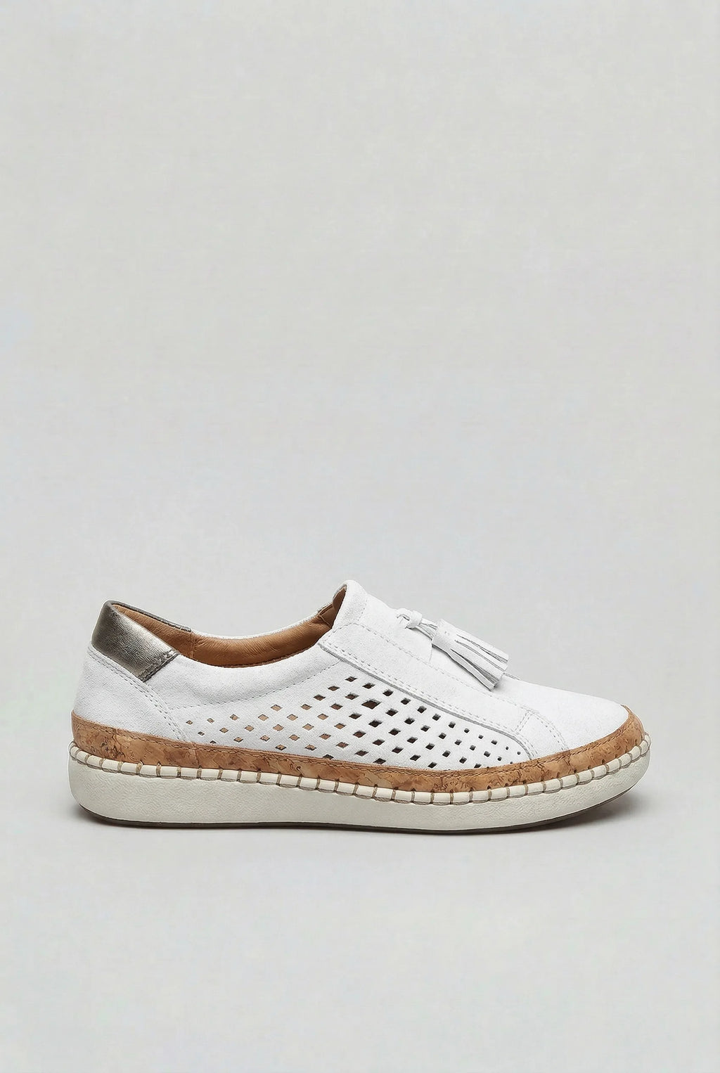 Side view of a white suede slip-on trainer with perforated cut-out design, tassel trim and cork platform sole