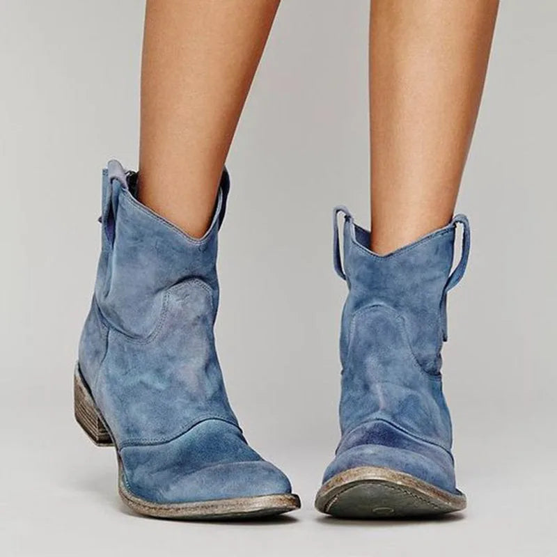 Blue suede ankle boots with side tabs and worn stacked heel, front facing view on bare legs
