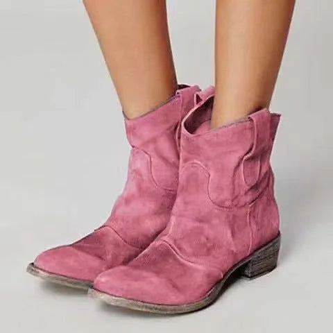 Pink suede ankle boots with rounded toe and distressed heel, front view on bare legs