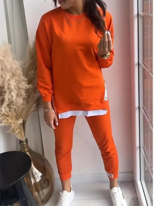 Orange sweatshirt and jogger set shown seated, with layered white hem and side zip pocket detail visible