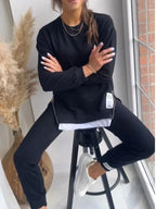 Black sweatshirt and jogger set worn while seated on a stool, showing the drop shoulder and tapered leg fit