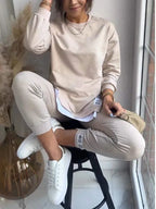 Beige sweatshirt and jogger set styled cross-legged, showing the ribbed cuffs and folded jogger hem