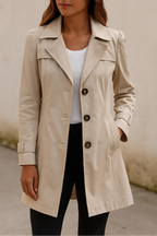 Front view of a beige tailored trench coat with notched collar, puff shoulders and button-front closure, worn open over a white top
