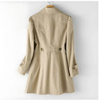Back view of the beige trench coat on a hanger, showing the fitted waist seam, back vent and buttoned cuffs