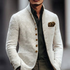 Man wearing a textured white stand-collar jacket over an olive shirt, styled with a bronze pocket square, front view