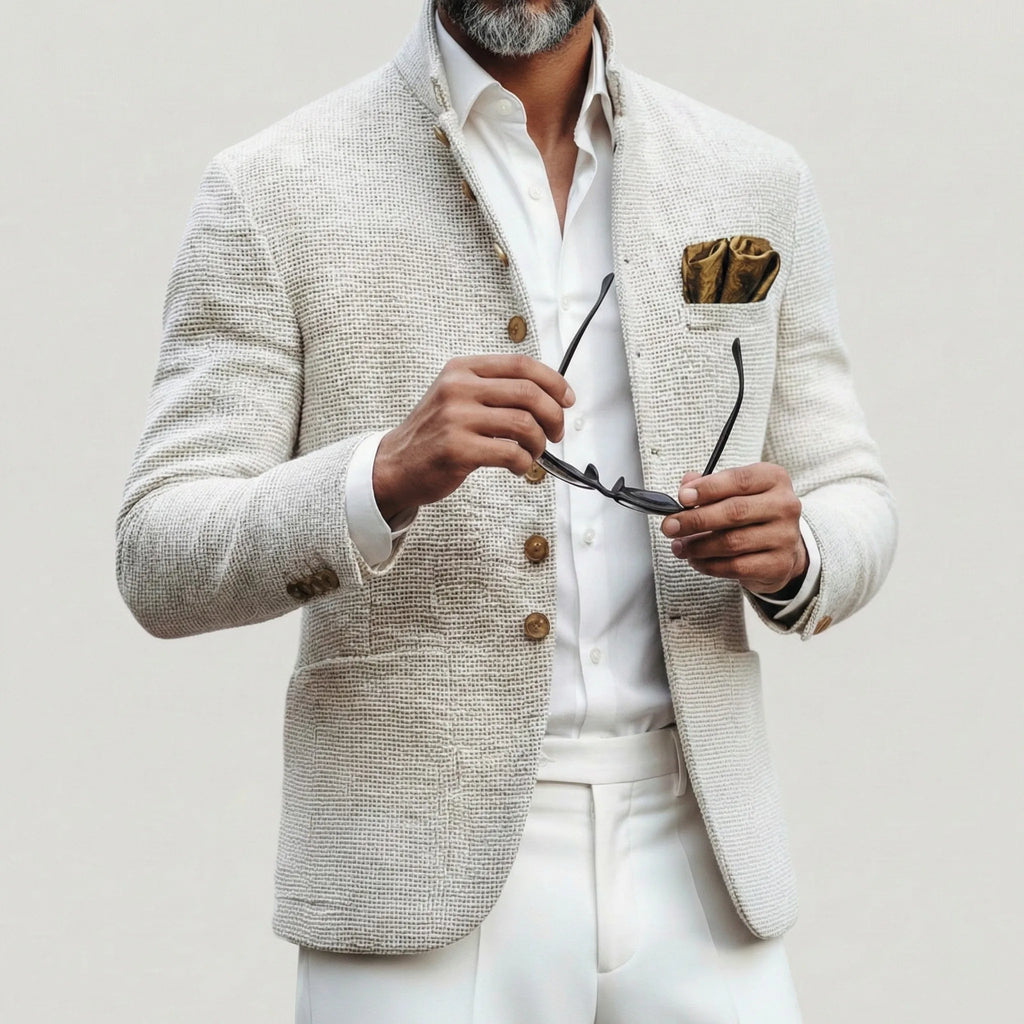 Older man in the white textured jacket buttoned over a white shirt, holding sunglasses, with white trousers