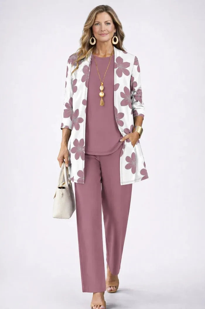 Woman wearing a mauve floral-print cardigan with matching dusty pink top and straight-leg trousers, holding a cream tote