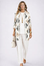 Woman wearing an ivory cardigan with black and tan leaf print, over a cream top and matching wide-leg trousers