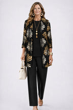 Woman in a black longline cardigan with gold and cream leaf print, paired with a black top and black trousers