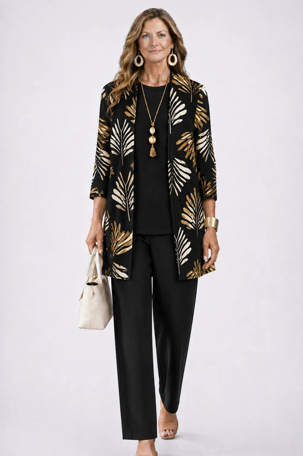 Woman in a black longline cardigan with gold and cream leaf print, paired with a black top and black trousers