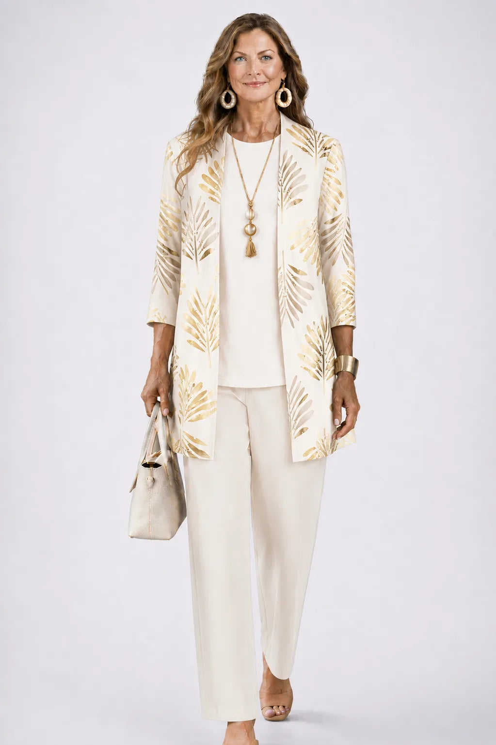 Woman in a cream cardigan with gold metallic leaf print, worn over an ivory top and matching trousers
